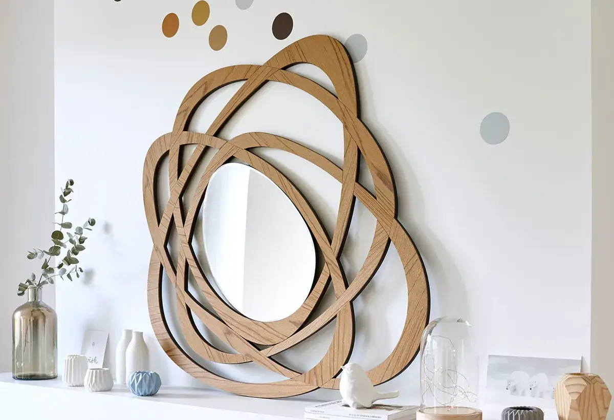 Miroir en bois aux formes entrelacées, une deco murale originale qui attire le regard. Des petits points colorés décorent le mur blanc.
