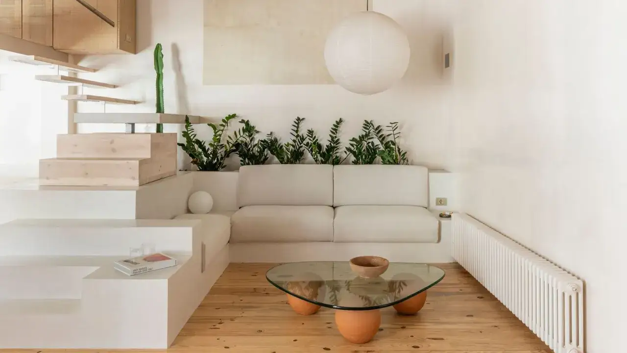 Salon au style wabi sabi, avec un canapé blanc, des plantes vertes, une table basse en verre et bois, et un escalier en bois brut.