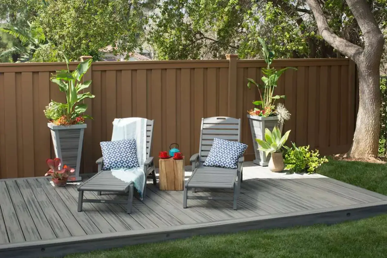 Aménager une petite terrasse sans se ruiner : deux chaises longues grises, coussins bleus, plantes en pots, table d'appoint en bois.