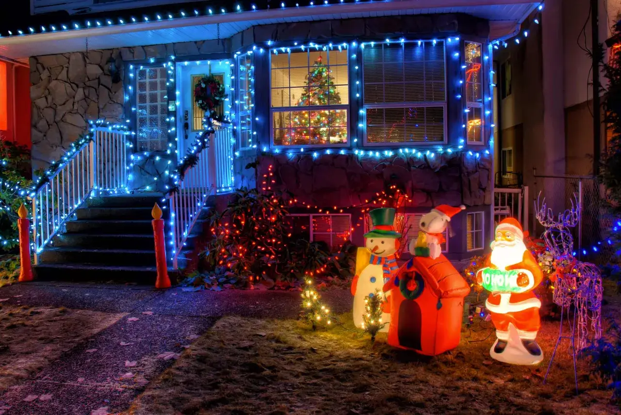La maison est décorée de lumières bleues et rouges, avec un Père Noël gonflable, un bonhomme de neige et un renne. C'est l'une des plus belles décorations de Noël extérieur.