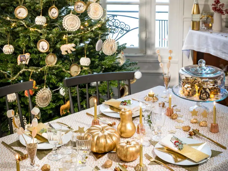 Déco table de Noël pas cher à faire soi-même : sapin décoré, citrouilles dorées, guirlandes lumineuses et vaisselle festive créent une ambiance chaleureuse.