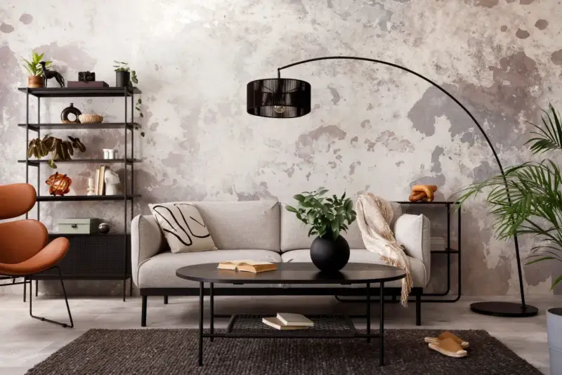 Salon industriel cocooning : canapé gris, fauteuil orange, étagère noire, table basse noire, tapis sombre, mur texturé.
