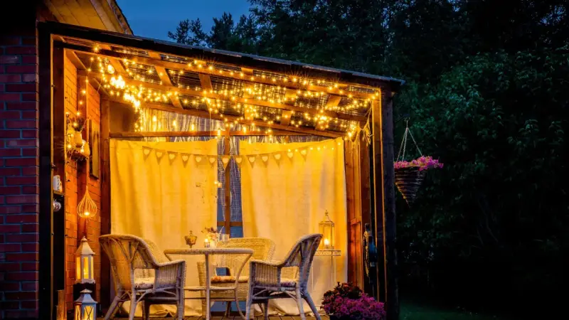 Une terrasse accueillante illuminée par des guirlandes lumineuses, une belle idée éclairage terrasse pour des soirées magiques. Meubles en rotin et fleurs ajoutent à l'ambiance.