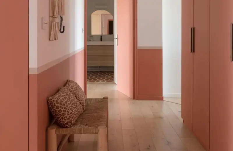 Banc en rotin avec coussins léopard, murs bicolores corail et blanc, portes roses. Une belle idée déco couloir moderne.