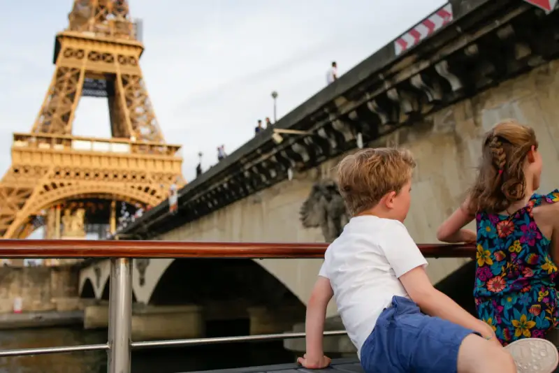 Deux enfants profitent d'une croisière sur la Seine à Paris la nuit, avec la Tour Eiffel illuminée en arrière-plan.